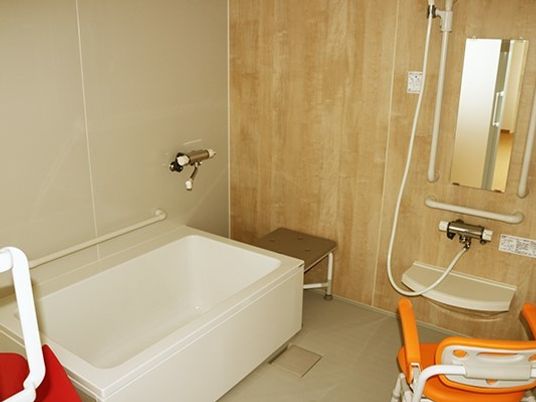 白い浴槽やシャワーが設置された浴室。ベンチや手すりも設置されている。