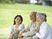 高齢夫婦と若い女性が座り、日当たりのいい芝生広場で楽しそうに話をしている。