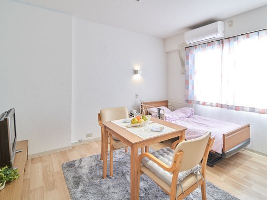 エアコンとテレビ、小さなテーブルやいす、ベッドが整ったワンルームタイプの部屋