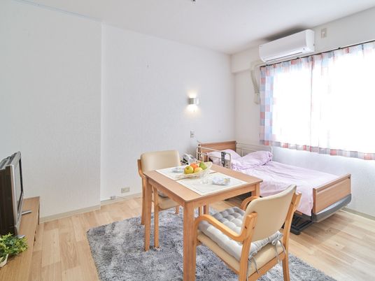 エアコンとテレビ、小さなテーブルやいす、ベッドが整ったワンルームタイプの部屋