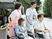 車いすの高齢の男女に付き添い、屋外で何かを鑑賞しているエプロンを付けた若い男女のスタッフ。