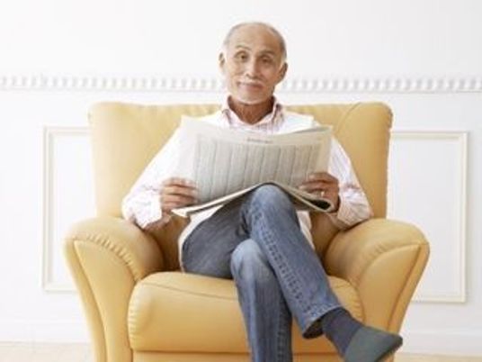 一人用のソファに座ってこちらを向いて微笑む男性。リラックスしている様子