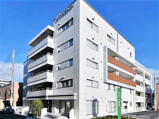 ５階建ての建物。白を基調とした清潔感のある外観で、すぐそばには広い駐車場もある。