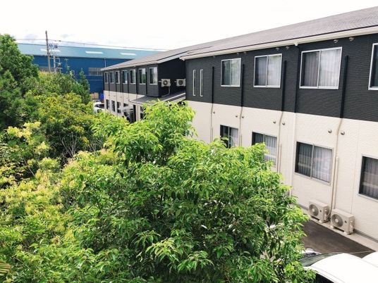 １階部分が白、２階部分がダークグレーのモノトーンの建物は緑に囲まれている。建物にはたくさんの窓が付き、敷地内には駐車スペースもある。