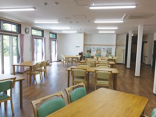 食堂にはグリーンや黄色の椅子が4人掛けのダイニングテーブルが並び、大きな窓にはレースカーテンとカーテンが付いていて、車いす対応の洗面所がある。