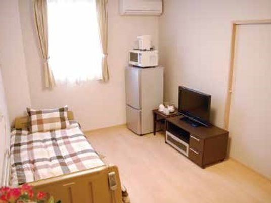 冷蔵庫や電子レンジ、テレビなどが置いてある小さな部屋の様子。窓やエアコンが付いているワンルーム