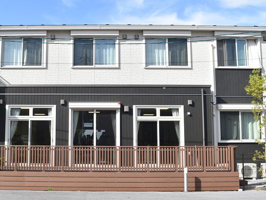 2階建ての建物。白とダークグレーで各フロアで外壁の色が異なり、植物も植えられている。