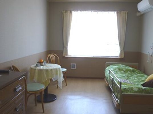 寝具付きのベッドやテーブルセットが置かれた部屋にはエアコンがあり、ベッドサイドには緊急通報装置もある。