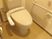 オレンジの呼び出しボタンや手すりが付いたトイレはシンプルなデザイン。トイレットペーパーホルダーもある。