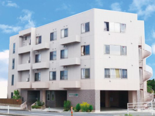 白を基調とした4階建ての建物は日当たりのいい場所に建っていて、屋外階段が付き、建物の周りには草木が植えられている。