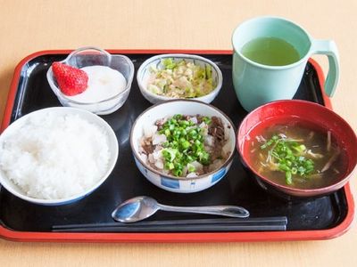 白いご飯にメインの肉料理、みそ汁やデザートまで付いた食事。黒いトレーには箸とスプーンも添えられている。