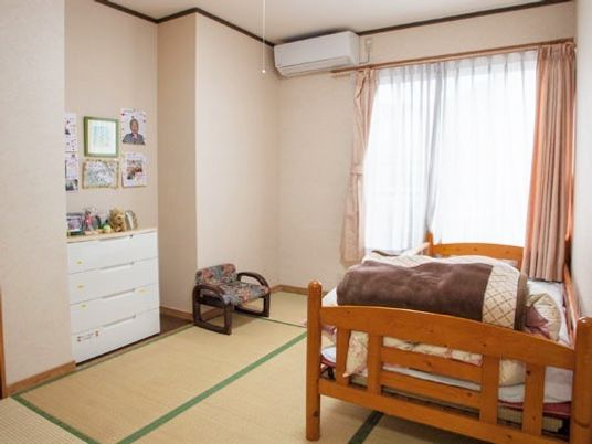 畳敷きの和室。落ち着いた雰囲気で介護ベッドやいす、エアコンなどが置かれている。