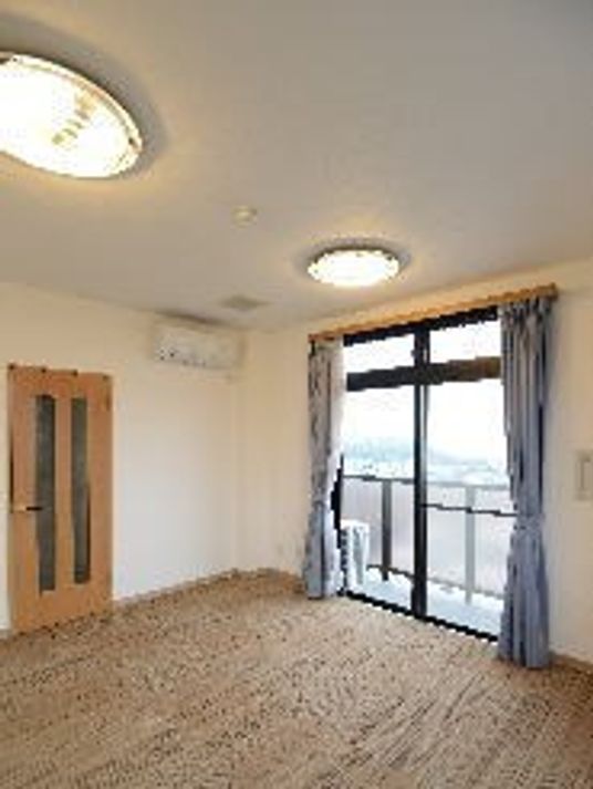 照明がついている小さなワンルームタイプの部屋。窓の外にベランダがある様子が分かる