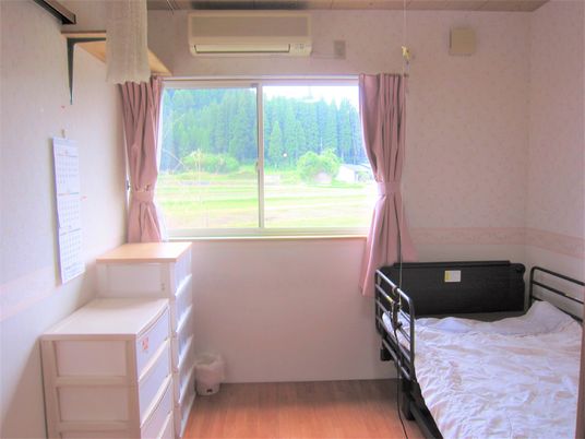 居室には寝具付きの介護ベッドやタンス、エアコン、カーテンなどが付き、窓の外には緑が広がっている。