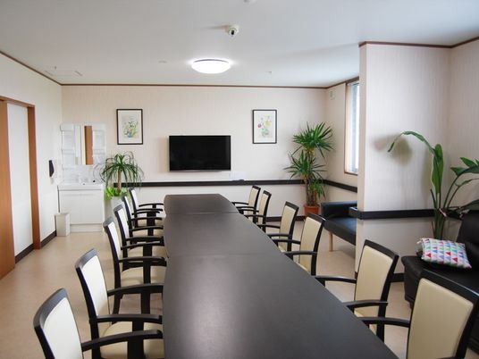 白と黒のダイニングテーブルセットが部屋の中央にあり、壁には壁掛けテレビ、観葉植物も多く置かれている。