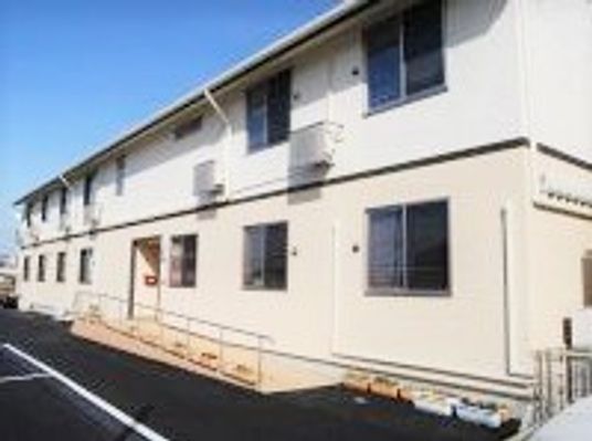 ２階建ての建物はベージュと白を基調とし、建物の中央にある玄関周りには手すり付きのスロープがある。