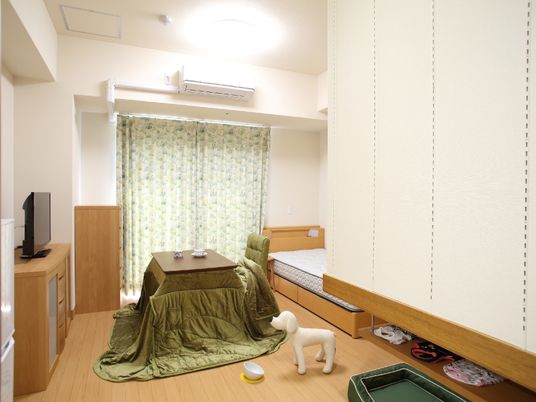 高めのこたつ、ベッド、テレビやタンスが写っている個室の様子