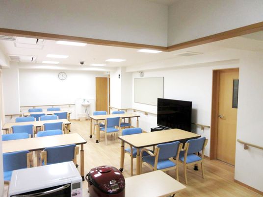 ブルーの椅子が設置された4人掛けのテーブルセットが複数置かれた食堂にはテレビや炊飯器もある。