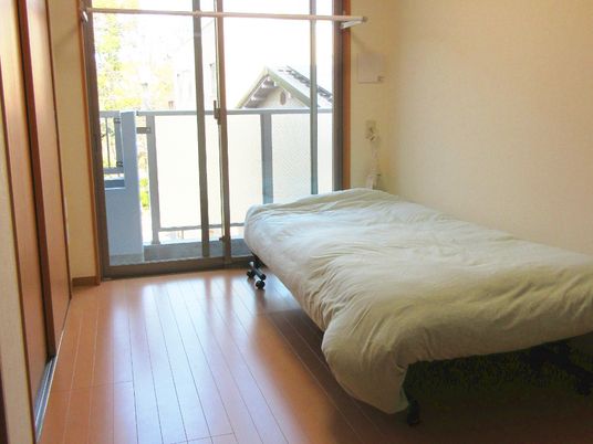 フローリングの部屋には寝具付きのベッドが置かれ、ベランダや緊急通報装置があり、明るい雰囲気。