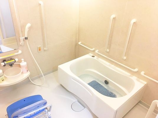 手すりが付いた一人用の浴槽が設置された浴室にはオレンジの呼び出しボタンやシャワーも付いている。