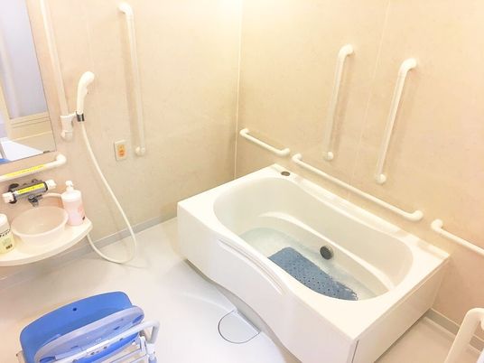 手すりが付いた一人用の浴槽が設置された浴室にはオレンジの呼び出しボタンやシャワーも付いている。