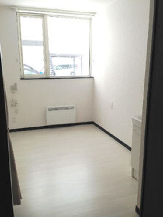大きな窓が付いたフローリングの部屋にはパネルヒーターと洗面所がある。窓にはカーテンはなく、家具や家電は置かれていない。