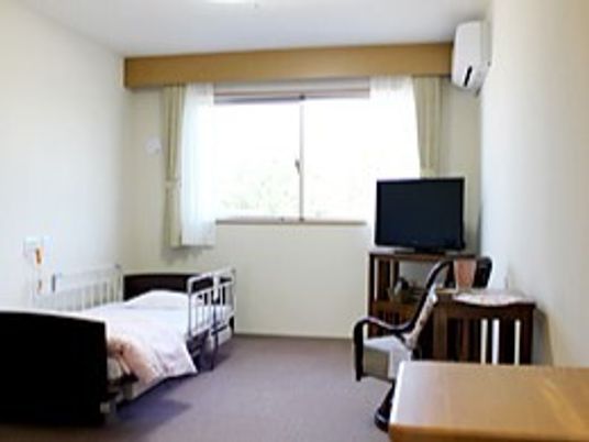 介護ベッドやテレビ、テーブルなどが置かれている部屋にはカーテンが付いた大きな窓があり、ベッドサイドには緊急通報装置がある。