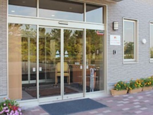 カラフルな花が植えられたプランターが設置されたエントランス周辺。マットが敷かれ、自動ドアが設置されている。