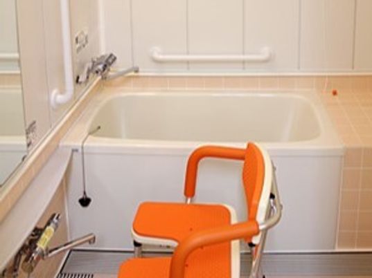 一人用の浴槽が設置されている浴室にはシャワーチェアや手すりがあり、壁には鏡も付いている。