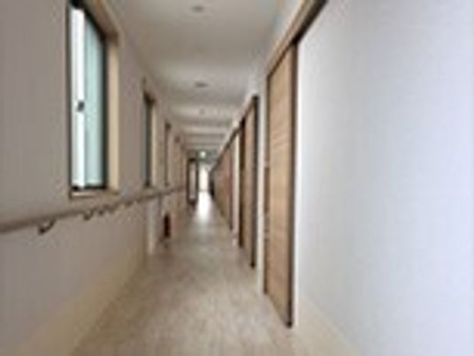 まっすぐな廊下の右側にはスライド式のドアが設置された居室が並び、左側には手すりが付いている。