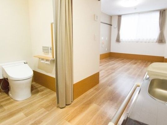 トイレやミニキッチンが付いたフローリングの居室。窓にはカーテンが付き、家具は置かれていない。