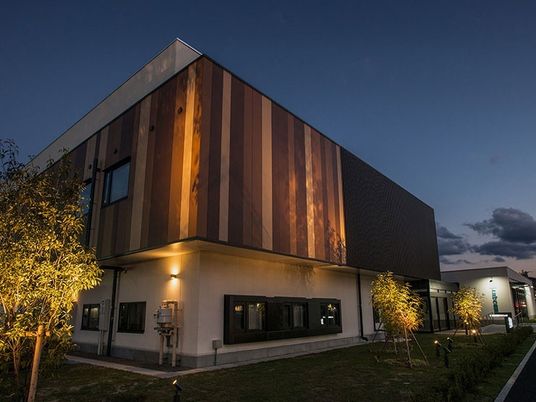 背の高い鉄骨造の建物の外観写真。やわらかい照明が外観を浮かび上がらせている様子