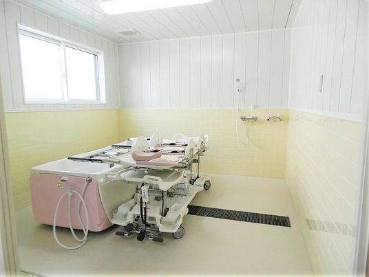 ピンクと白の機械浴槽が設置された浴室はタイルが貼られ、明るい雰囲気。