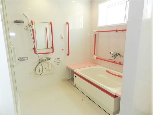 白い浴槽に設置されたピンクのベンチと赤い手すりがよく映える。