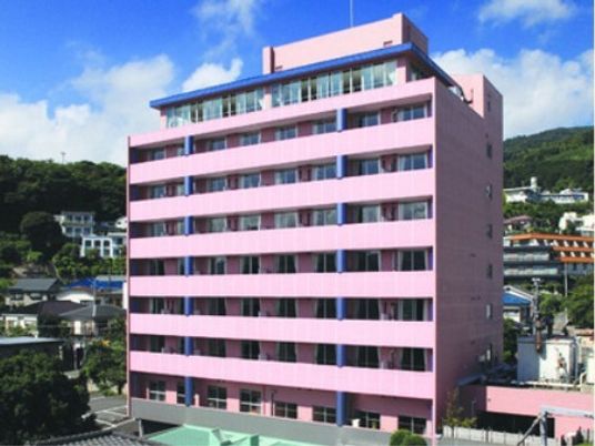 ピンクの大きな建物は高層マンションのような外観。周辺にも住宅が多く、遠方には山も見える。