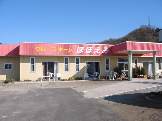 ピンクの屋根が印象的な平屋建ての建物。日向ぼっこができるようにとたくさんのいすが置かれている。