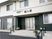 モノトーンの2階建ての建物の玄関には階段とスロープが付き、ホーム名と併設のデイサービスの名前が書かれている屋根も設置されている。