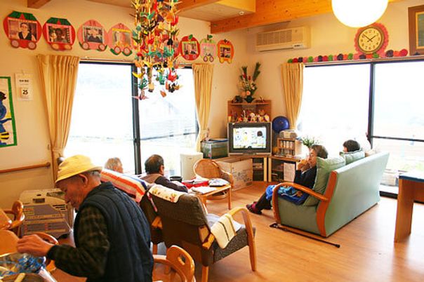 明るい雰囲気のリビングダイニングでテレビ鑑賞や工作をしてくつろぐ入居者たちの様子。