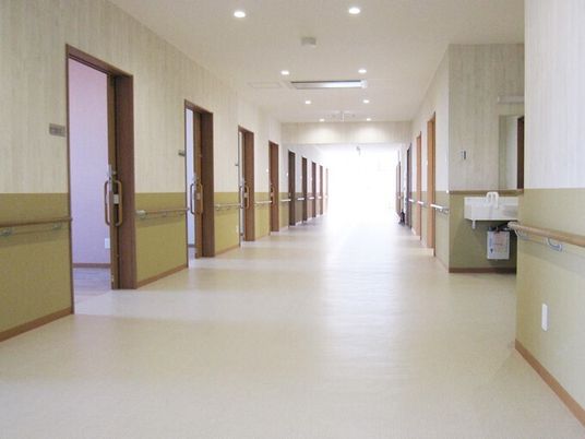 幅が広い施設内の廊下の様子。手すりがついた廊下の壁と個室の入り口