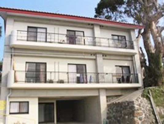 3階建ての建物は白を基調としていて、ベランダが各フロアにつき、周辺には自然も残されている。