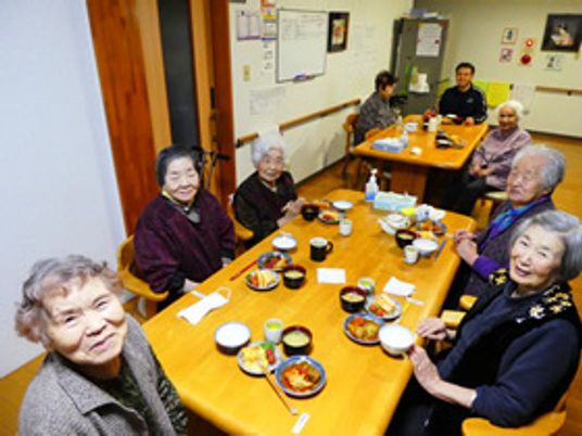 家庭的なサイズの食卓を囲み笑みを浮かべる入居者たち。おいしそうな食事が並んでいる。