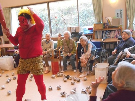 赤鬼に扮したスタッフに向かって髪を丸めたボールを投げている高齢女性たち。