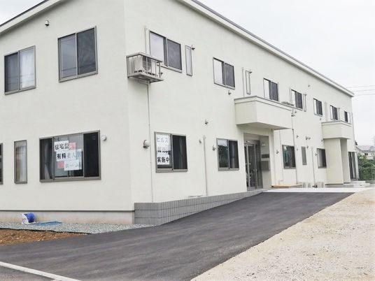 白を基調とした2階建ての建物は玄関に屋根が付き、窓も多い。