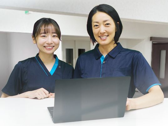 笑顔でパソコンの前に立っている2名の紺のユニフォームを着た女性スタッフ。