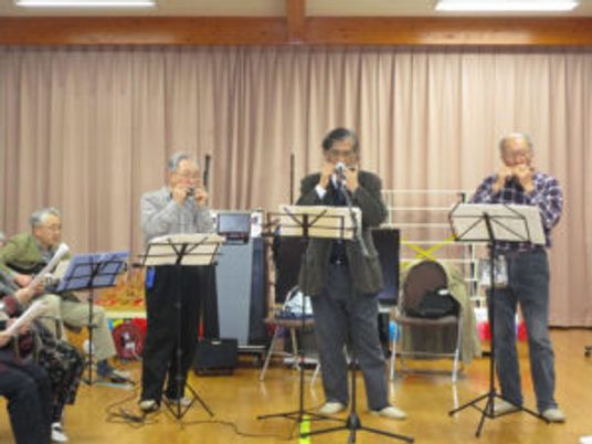 ハーモニカやギターを演奏する高齢の男性グループ。どなたも眼鏡をかけている。