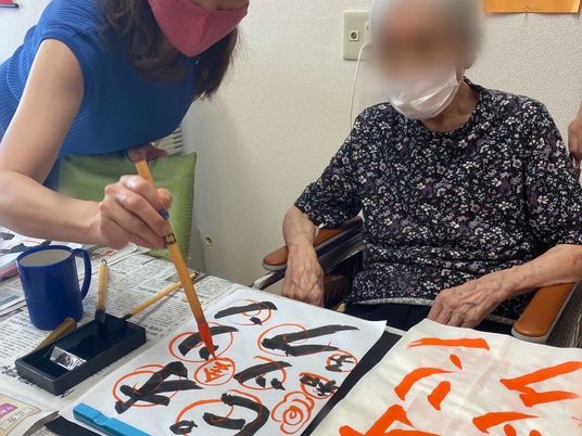 書道をしている高齢女性。オリンピックと書かれた半紙にはたくさんの丸が付いている。