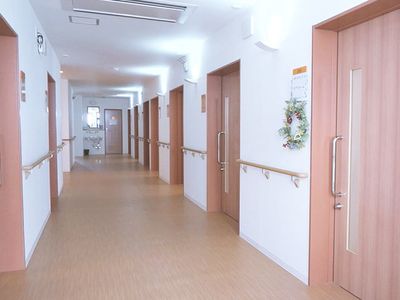 手すりがついた壁と個室のドアが並んでいる施設内の廊下の様子