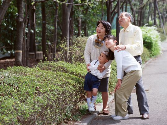 孫や子供たちと一緒に散歩している高齢者夫婦。天気が良い日の公園の一場面