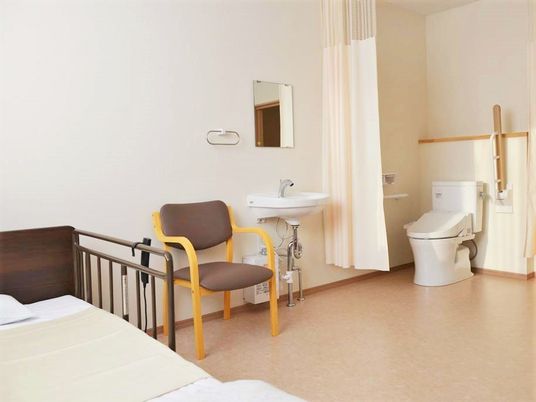 ベッドと椅子、洗面台、ドアレスのトイレがついている施設内の居室の様子