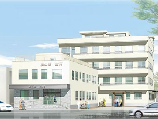 白を基調にした4階建ての大きな建物、玄関周りにはスロープが付き、スタッフと入居者が数名歩いている。